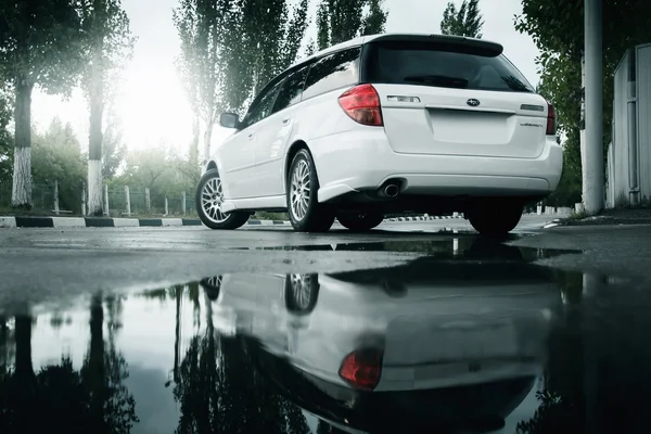 Car Subaru Legacy se queda en la carretera de asfalto y se refleja en el charco en la ciudad durante el día — Foto de Stock