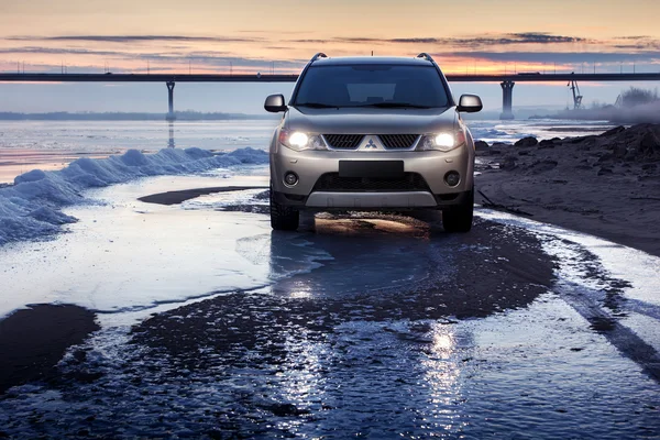 Car Mitsubishi Outlander permanecer en la costa de hielo al atardecer de invierno — Foto de Stock