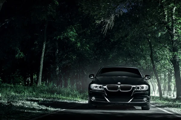 Coche negro BMW E90 de pie en la carretera en la oscuridad del bosque por la noche —  Fotos de Stock