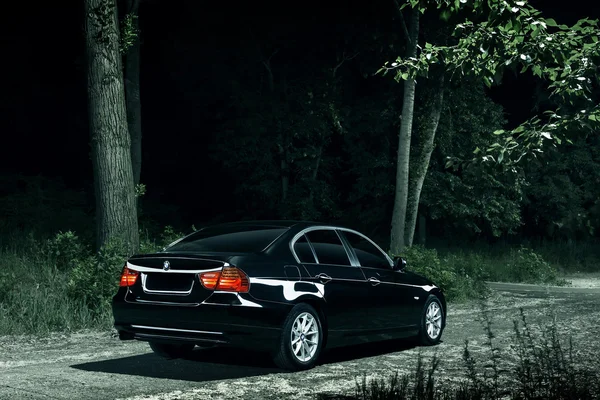 Coche negro BMW E90 de pie en la carretera en la oscuridad del bosque por la noche —  Fotos de Stock