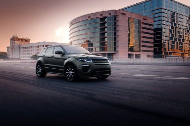 Gün batımında şehir Moskova'da asfalt yolda araba Land Rover Range Rover Evoque ayakta