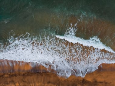 Okyanus dalgaları ve kırmızı kumsal havadan görünüyor. Mavi deniz suyu arka planı