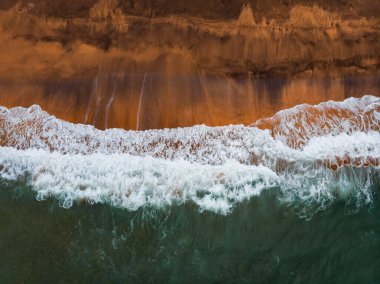 Okyanus dalgaları ve kırmızı kumsal havadan görünüyor. Mavi deniz suyu arka planı