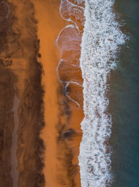 Okyanus dalgaları ve kırmızı kumsal havadan görünüyor. Mavi deniz suyu arka planı