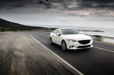Araba sürat deniz kıyısındaki yolda bulutlu gökyüzü manzarasında mazda