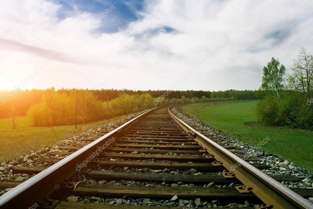 Railway tracks on green summer landscape at sunset