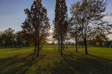 Zagreb 'deki Jarun Gölü kıyısında gün batımının güzelliği, insanların dışarıda yürüyüp güneşin tadını çıkarması.