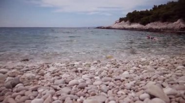 Hvar adasındaki güzel çakıl taşlı plajda, sığ sularda yüzen ve eğlenen turistler var.