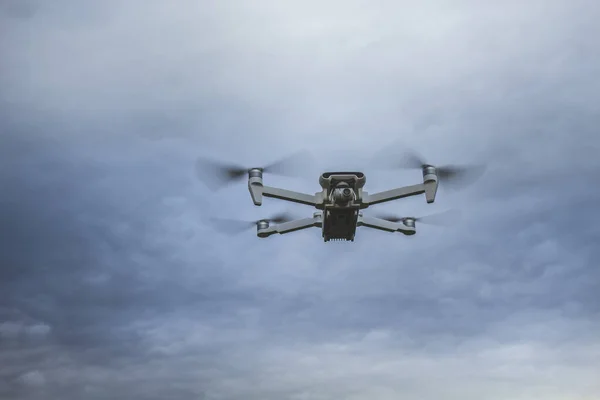 White drone hoovering in the sky, photographed against the cloudy, sunset sky