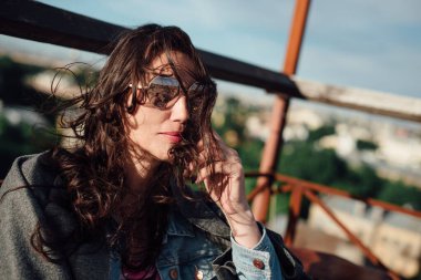 Orta yaşlı güzel bir kadın elinde bir fincan kahveyle çatıdaki bir kafede oturuyor..