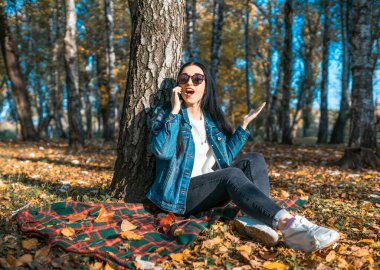 Sarı bir sonbahar parkında cep telefonuyla konuşan çekici genç bir kadın. Tatlı bir kız güneşli bir sonbahar gününde dışarıda yürürken arkadaşlarıyla telefonda iletişim kurar. Uzaklık iletişimi kavramı