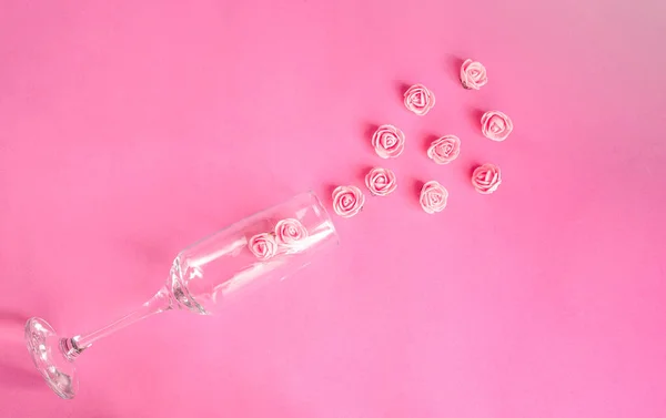 Pembe arka planda küçük parlak güller serpiştirilmiş şampanya bardağı. Sevgililer Günü kutlaması konsepti. Tatilin romantik atmosferi. kopyalama alanı. Düz yatıyordu. en üstteki görünüm