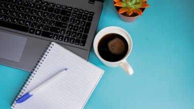 Ofisteki işyerinde mavi bir arka plan var. Dizüstü bilgisayar, akıllı telefon, not defteri, kalem, bardak, sulu bitkiler ve koyu kahve. İş ve Finans kavramı. Boşluğu kopyala