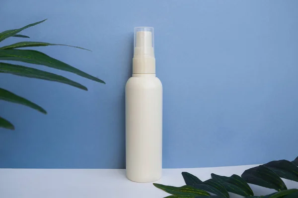 Mockup of cosmetic spray, bottle packaging on a blue background, face, hair and body skin care with tropical leaves. copy space