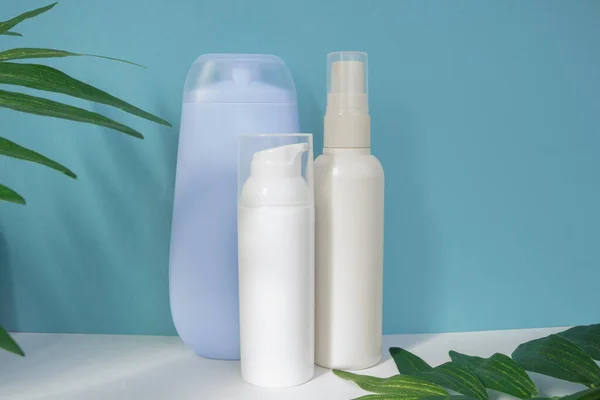 White and blue cosmetic bottles for skin care on a blue background with tropical leaves. Bio cosmetic products packaging design. Promotional cosmetic product. Sun protection concept. Copy space