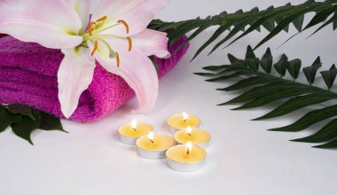Havlulu spa seti, zambak çiçeği, bir grup mum, beyaz arka planda tropik yapraklar. Spa ve rahatlama konsepti. Boşluğu kopyala