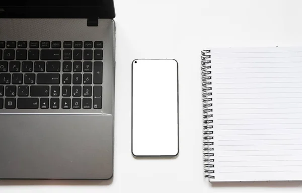 Bilgisayarlı modern beyaz ofis masası, beyaz ekranlı akıllı telefon, not defteri. İş ve Finans kavramı. Uzayı kopyala en üstteki görünüm