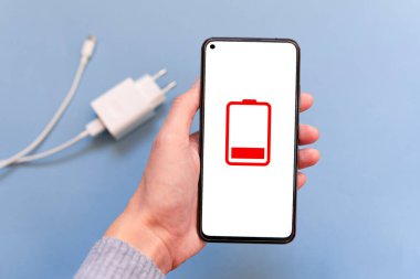 Ekranda yerleştirilmiş bir pil simgesi olan Smartphone 'u elinde tutuyor. Bir akıllı telefonu USB kablosu ve mavi arka planda güç kaynağı ile şarj etmek. Taburcu edilmiş telefon konsepti. Boşluğu kopyala