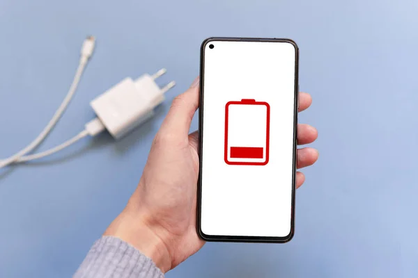 画面上の上部ビューに植えられたバッテリーアイコンを持つスマートフォンを保持しています Usbケーブルと青い背景の電源を介してスマートフォンを充電します 放電電話の概念 スペースのコピー — ストック写真