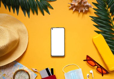 Seyahat aksesuarları, akıllı telefon ekran modeli, gözlükler, tıbbi maske, açık sarı arka planda mesaj için boş alan olan parlak sarı bir şapka. Seyahat ya da akıllı telefonlu tatil konsepti. Düz yatıyordu. 