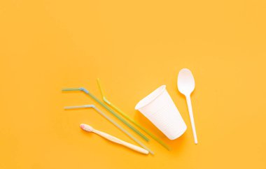 Plastik atık, fincan, kaşık, plastik diş fırçası, sarı arka planda pipet koleksiyonu. Plastik ve ekoloji geri dönüşüm konsepti. Düz yerde, üst tarafta. Boşluğu kopyala