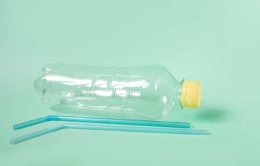 Yeşil arka planda tek kullanımlık plastik şişe ve saman, ekolojik ayrılık kavramı ve plastik atık koleksiyonu. Plastiği reddetmek. Metin için alanı kopyala
