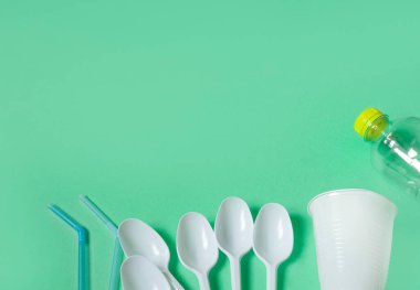 Çeşitli tek kullanımlık plastik atıklar, kaşıklar, yeşil arka planda şişeler, ekolojik ayrılık kavramı ve plastik atık koleksiyonu. Plastiği reddetmek. Yukarıdan bak. Düz yatıyordu. metin için boşluk kopyala