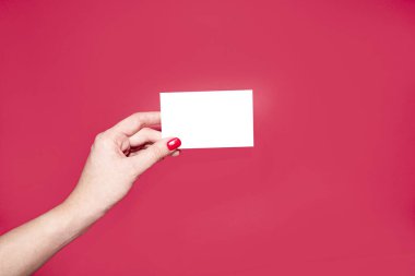 Güzel manikürlü bir kadın elinin altında indirim kartı, kartvizit ve kırmızı arka planda beyaz bir kağıdın kopyası var. Tasarım şablonu. Yerleşim planı. metin için boşluk kopyala