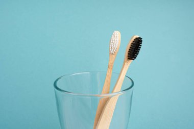 Doğal çevre dostu bambudan iki diş fırçası bir bardakta, mavi arka planda yakın plan. Sürdürülebilir yaşam tarzı, geri dönüşüm ve ekoloji kavramı. metin için boşluk kopyala