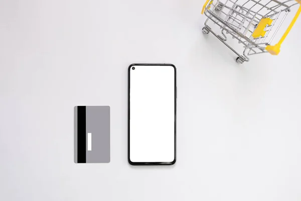 Beyaz ekran maketli akıllı telefon, gümüş kredi kartı, beyaz arka planda izole edilmiş alışveriş arabası. Çevrimiçi alışveriş, ev teslimatı, kara cuma, indirim. Düz konum, üst görünüm, metin için boşluk kopyala