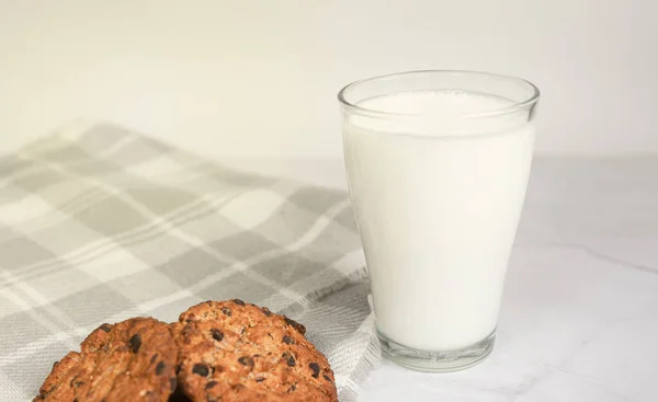 A glass of milk, chocolate oatmeal cookies and crumbs on a white plate in the rays of the sun. Tasty breakfast. The concept of proper nutrition and weight loss. copy space for text