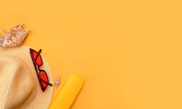 Hasır plaj şapkası, güneş koruyucu krem, kırmızı güneş gözlüğü, sarı arka planda deniz kabukları. Denizde tatil kavramı, turizm, seyahat. Yaz modası, tatil. Metnin için boşluk kopyala. en üstteki görünüm
