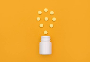 İlaç kapsülleri sarı arka plandaki beyaz bir şişeden yayılmış. İlaç, ağrı kesici, antibiyotik, vitamin. Vitamin hapları sarıdır. Sağlık sigortası ve ilaç. Düzdü. en üstteki görünüm