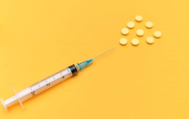 Sarı arka planda şırınga ve haplar. Yüksek doz, vitamin, şırıngadan çıkan sarı haplar. Vitamin kompleksi konsepti, sağlık, güzellik ve gençlik vitaminleri. 
