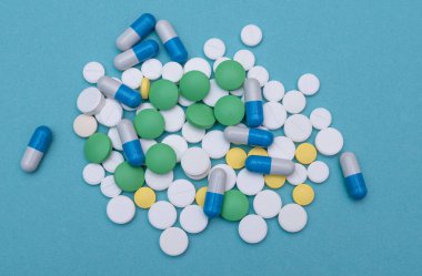 Açık mavi arkaplanda, sarı, yeşil, mavi ve beyaz renkli farklı tabletlerden oluşan bir grup. İlaç, ilaç tedavisi ve çeşitli hastalıklar için antibiyotik konsepti. en üstteki görünüm