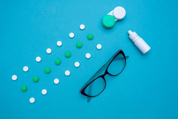 Görme yetisini, tabletleri ve vitaminleri, göz damlalarını, kontak lensleri, mavi arka plandaki görüşü iyileştirmek için gözlük. Doktor 'un masası. Göz ve görüş tedavisi konsepti. en üstteki görünüm. 