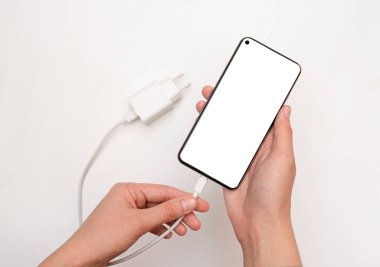 Akıllı telefonu USB kablosu ve güç ünitesini beyaz arka planda şarj etmek, USB kablosu bağlamak, üst görünüm. Beyaz ekranlı akıllı telefon. USB kablosu ile şarj edilebilir akıllı telefon kavramı.