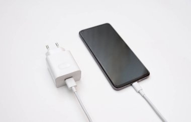Bir akıllı telefonu beyaz arka plan, üst ve yan görüntü üzerinden USB kablosuyla şarj etmek. Beyaz boş alana USB kablo ve güç kaynağı yüklü siyah akıllı telefon silueti. Kopyalama uzayı. seçici odak