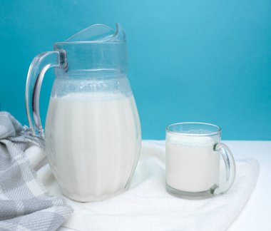 Beyaz ve mavi arka planda bir sürahi ve bir kupa taze süt. Çiftlik ürünü konsepti. Dünya Süt Günü. Sağlıklı beslenme. metin için boşluk kopyala