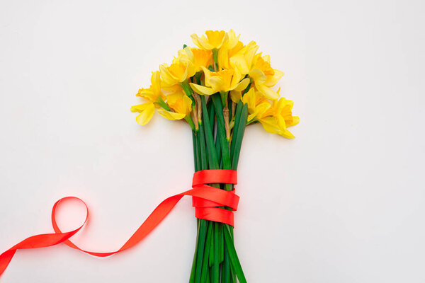 Bouquet of yellow daffodils tied with an orange ribbon on a white background. Mother's Day, International Women's Day, Spring is coming. copy space for text. Flat lay, top view