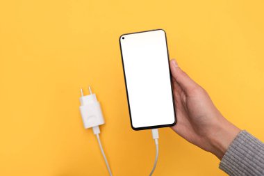 Bir akıllı telefonu USB kablosuyla şarj etmek ve sarı arka plandaki güç ünitesi şarj cihazına bağlamak. Beyaz ekranlı akıllı telefon. Üstten görüş, iş ve teknoloji. Boşluğu kopyala
