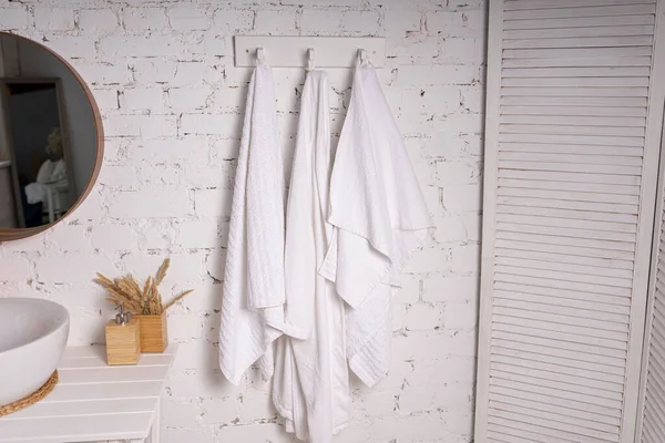 Beyaz havlular, banyo aksesuarları beyaz bir duvarda asılı havlular. Spa konsepti, otel servisi