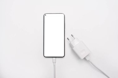Beyaz ekran maketi ve güç kaynağı olan akıllı telefon, beyaz arka planda şarj aleti. Telefonun bataryasını şarj etmek için USB kablosu. Üst görünüm, düz görünüm, metin için boşluk kopyala