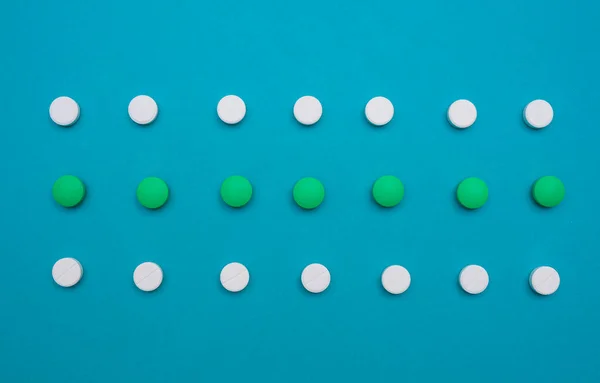 Various white and green pills and tablets, capsules are laid out in a straight line on a blue background. Concept of the pharmaceutical industry and medicines. Flat lay. top view. copy space for text