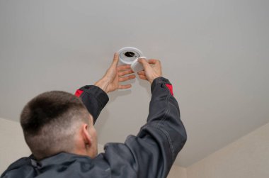 Bir elektrikçi gergin bir tavana spot ışığı yerleştirir ya da değiştirir. Bir elektrikçi tavana modern LED lambalar takıyor. Enerji tasarrufu teknolojisi kavramı. Bir elektrikçi çalışıyor. Boşluğu kopyala