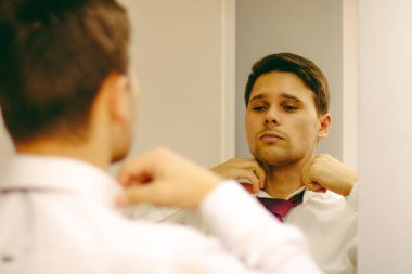 Adam aynada kravatı ayarlar. Beyaz gömlekli adam aynadaki kravatı düzenler..