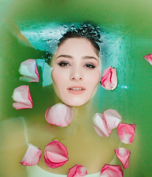 Küvette renkli suyu olan bir kız. Küvette gül yapraklı bir kız. Küvette yeşil suyu olan bir kız. Çiçeklerle dolu sağlık banyosu