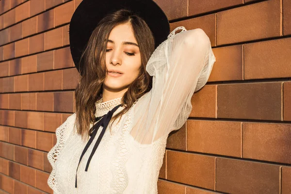 Tuğla duvardaki kız. Arka planda şapkası olan kız