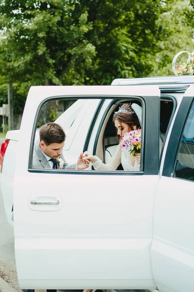 Gelin ve damat limuzinden iniyorlar. Damat gelinin arabadan inmesine yardım eder.