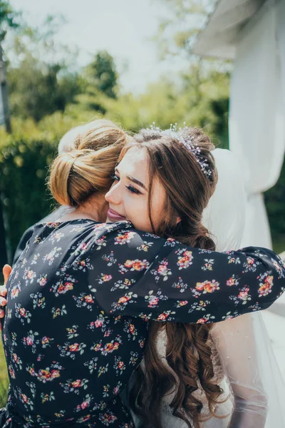 Anne kızını kucaklıyor. Anne geline sarılır.